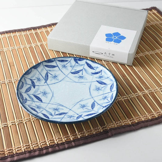 A small blue-and-white plate painted with balloon flowers, beside its gift box on a bamboo mat