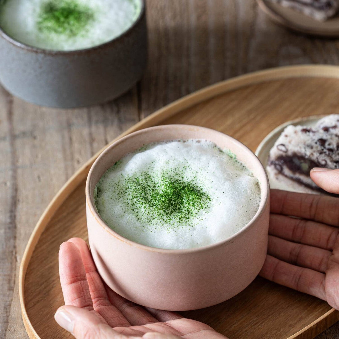 A frothy matcha latte in a dawn-pink porcelain cup, held in two hands